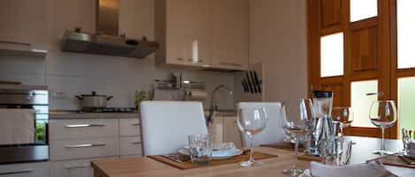 A modern kitchen with white cabinets, a wooden table set for dining, and a view of the outdoors through a window.