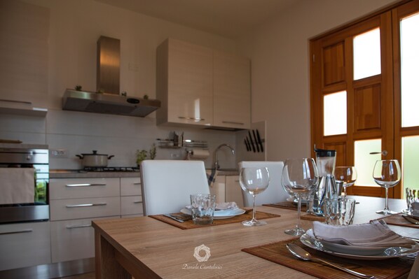Una cocina moderna con armarios blancos, una mesa de madera lista para comer y vistas al exterior a través de una ventana.