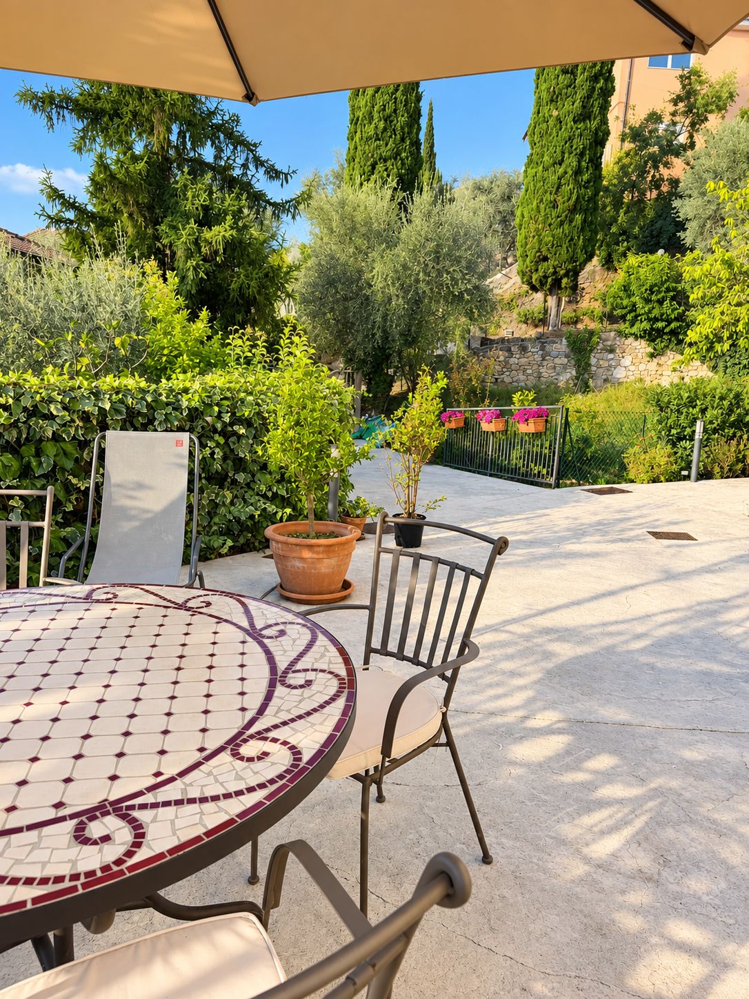 Une terrasse extérieure avec une table ronde, deux chaises, un pot de fleurs et une clôture en métal.