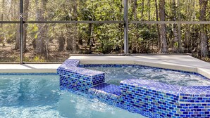 Une piscine aux carreaux de mosaïque bleus, agrémentée d’une cascade, et entourée d’une zone boisée.
