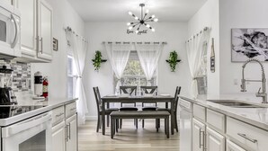 Une cuisine moderne avec des meubles blancs, une table à manger avec des chaises et un lustre.