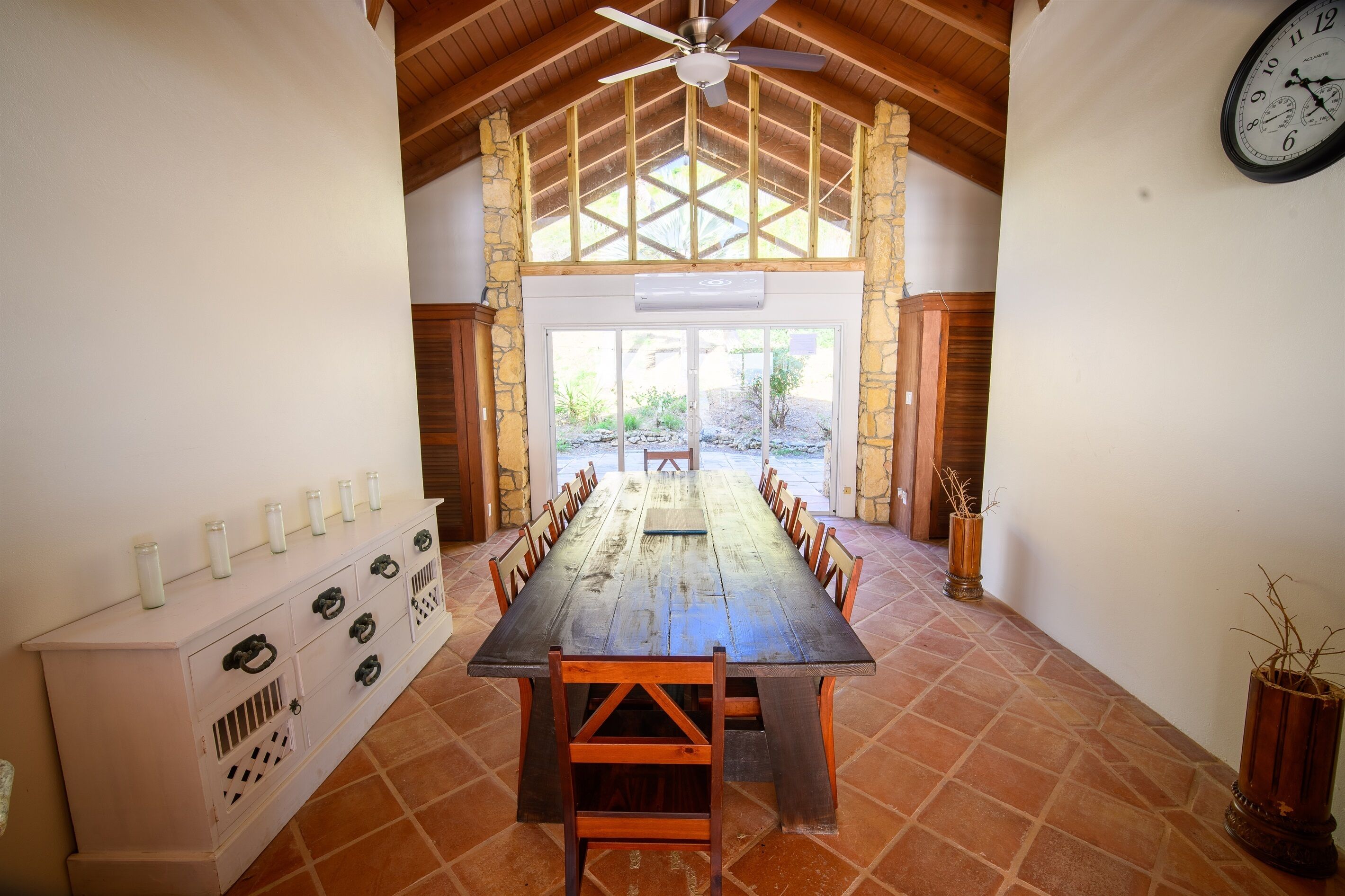 A long wooden table with chairs, a white console with drawers, and a clock on the wall.