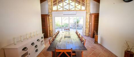 A long wooden table with chairs, a white console with drawers, and a clock on the wall.