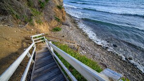A wooden staircase leading down to a rocky beach with ocean waves.