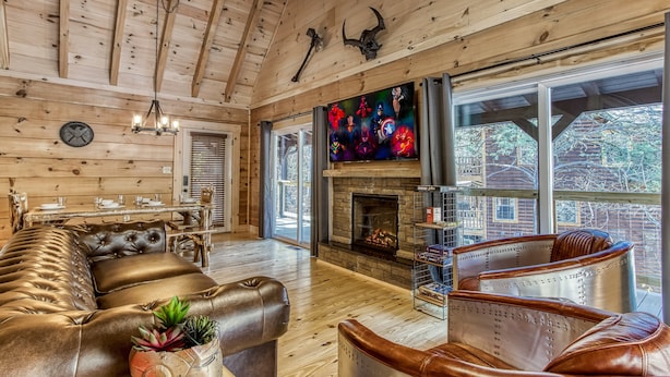 A spacious living room with a fireplace, leather furniture, and a large window offering a view of the outdoors.