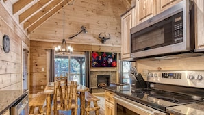 A modern kitchen with wooden cabinetry, a built-in microwave, a stove, and a dining area with rustic benches.
