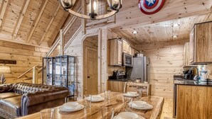 A wooden interior with a dining table set for six, a leather sofa, and a kitchen area with a microwave.