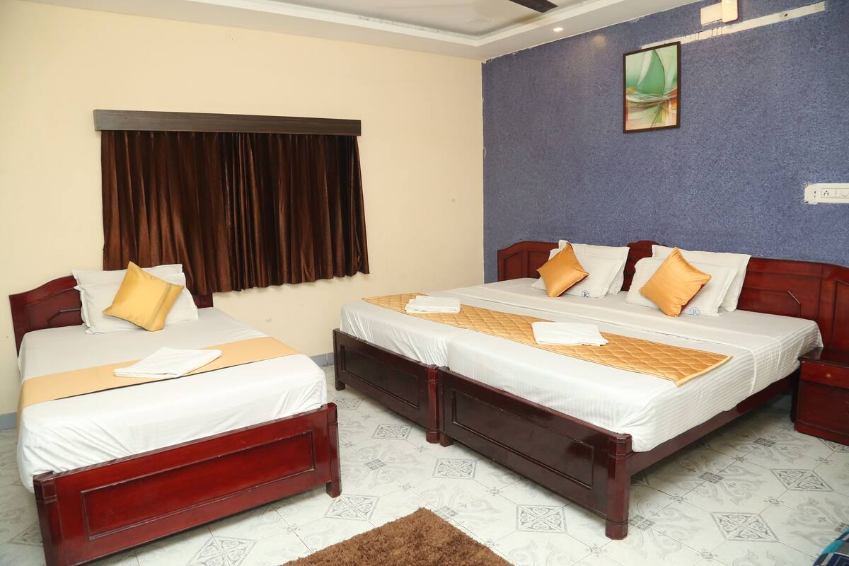 A hotel room with two beds, a large window with curtains, a wall-mounted painting, and a patterned floor.