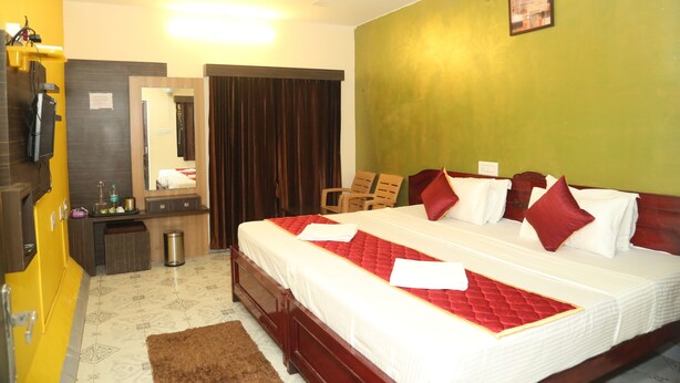 A hotel room with a large bed, a wooden dresser, a mirror, a desk, and a trash can. -  LA FLORA RESORTS YERCAUD (Yercaud)