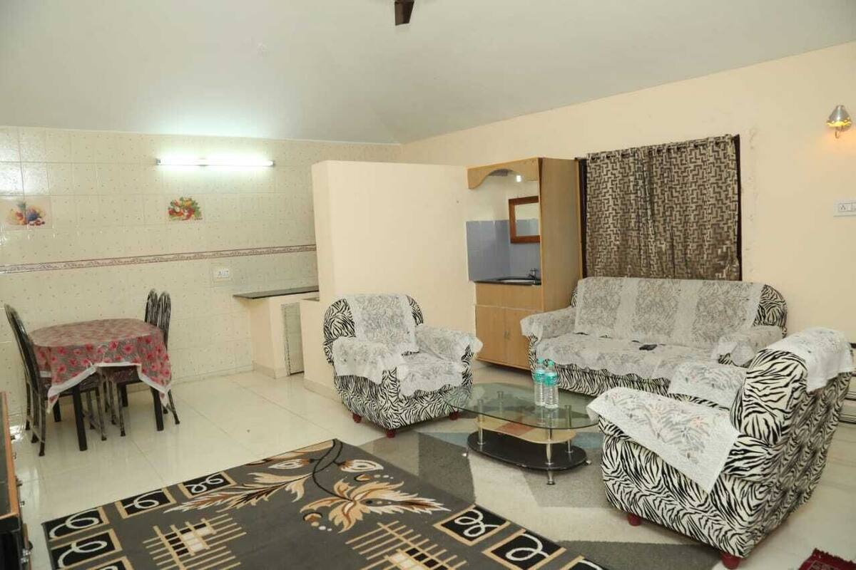 A living room with two patterned sofas, a glass coffee table, a dining table with chairs, and a patterned rug.