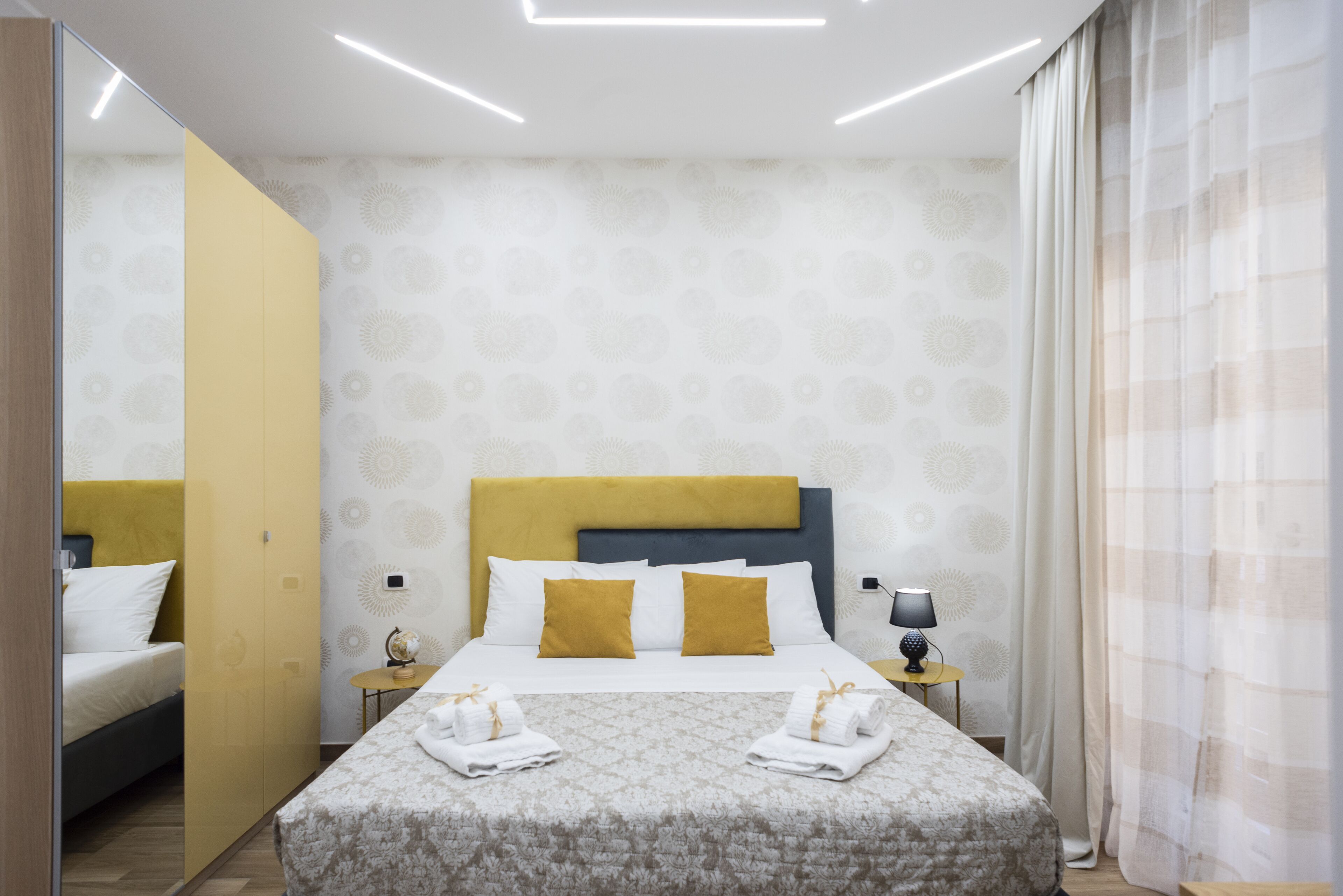 Una habitación de hotel moderna con cama, mesita de noche, lámpara y espejo.