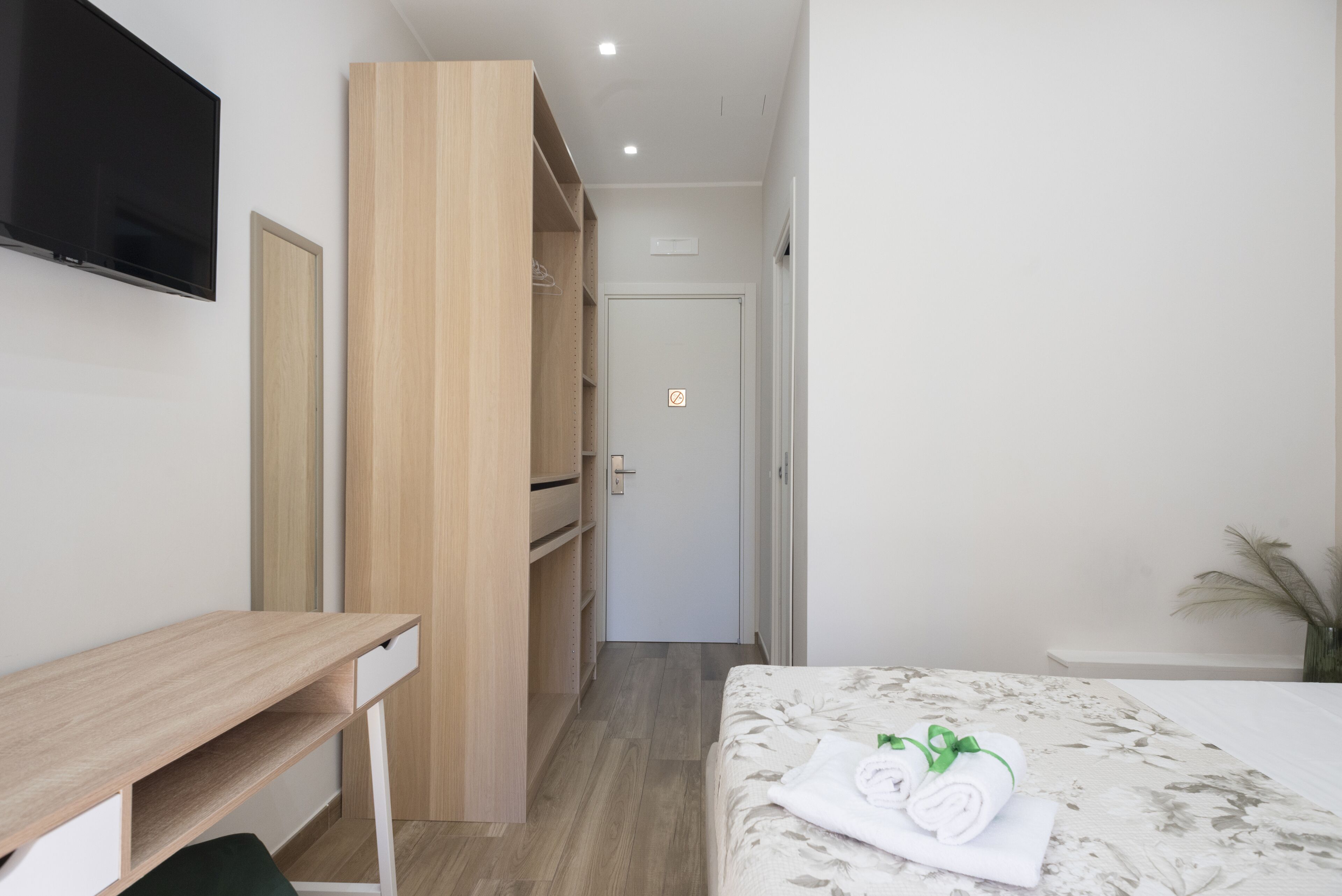 A hotel room with a wooden desk, a bed with a floral bedspread, and a TV mounted on the wall.