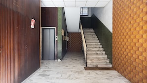 Uma escadaria com piso de mármore que leva a uma porta com sinal de saída de incêndio.