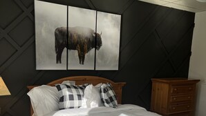 Camera da letto con un letto grande, un comodino con una lampada, una cassettiera in legno e un quadro appeso al muro raffigurante un bisonte.