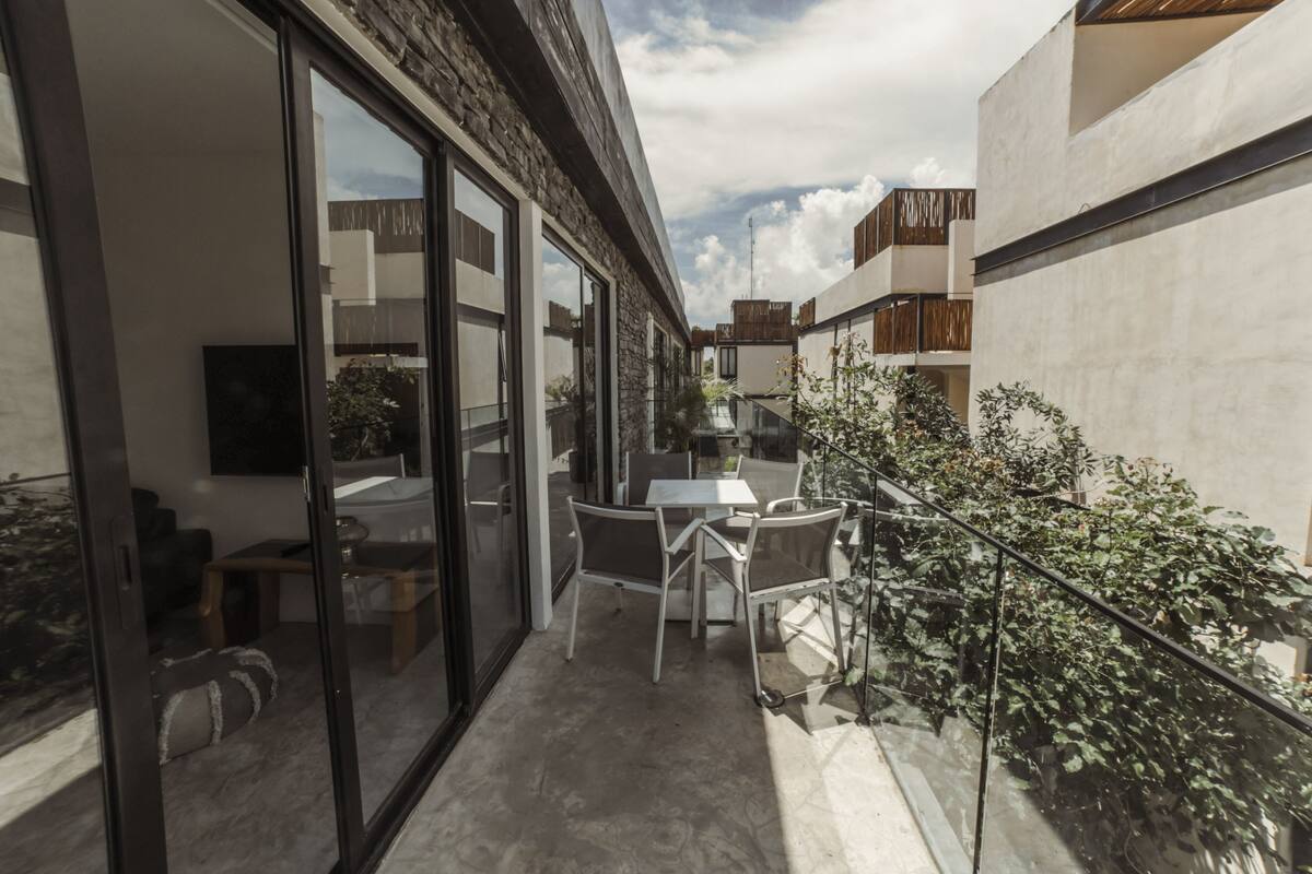 A modern outdoor patio with a glass door leading to a living area, a small table with chairs, and a potted plant.