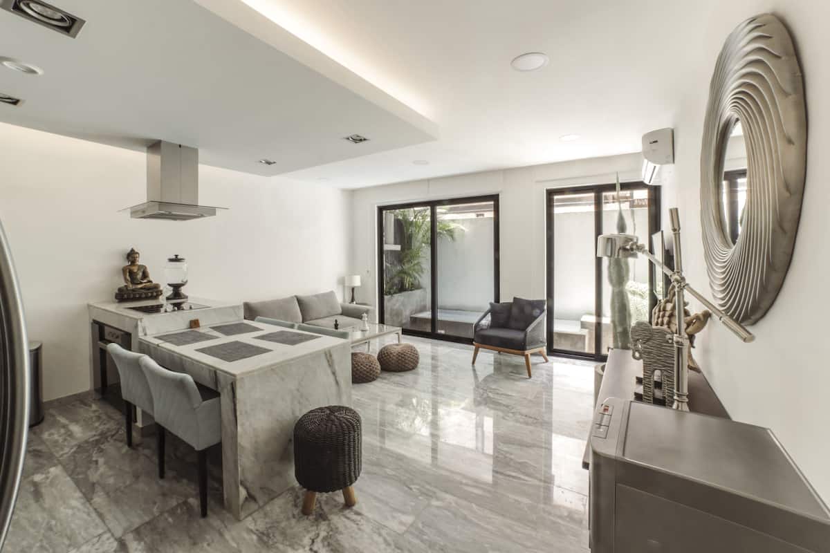 A modern kitchen with a marble countertop, a dining area with a table and chairs, and a large decorative mirror on the wall.