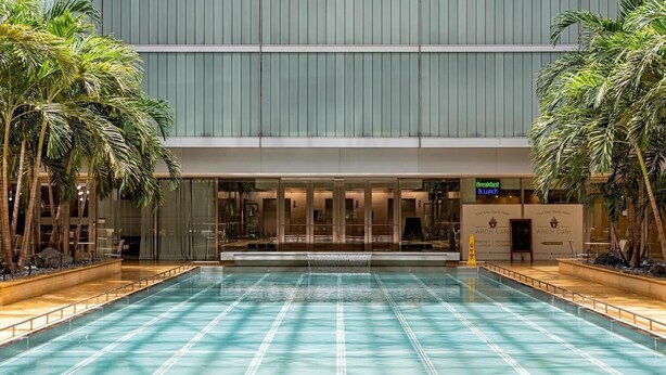A swimming pool with a glass bottom, surrounded by palm trees and a building with a modern design. - Luxury Brickell Bay View Condo AKA Hotel 33rd Floor (Miami)