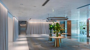 A modern hotel lobby with a long corridor, round tables with green plants, and a glass wall with a digital display. - Luxury Brickell Bay View Condo AKA Hotel 33rd Floor (Miami)