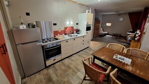 Eine kompakte Küche mit Gasherd, Backofen und modernen Geräten. Es gibt einen Essbereich mit einem Holztisch und Korbstühlen.