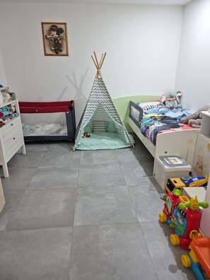 Une chambre d’enfant avec deux lits, un espace de jeu avec des jouets et un tableau accroché au mur.