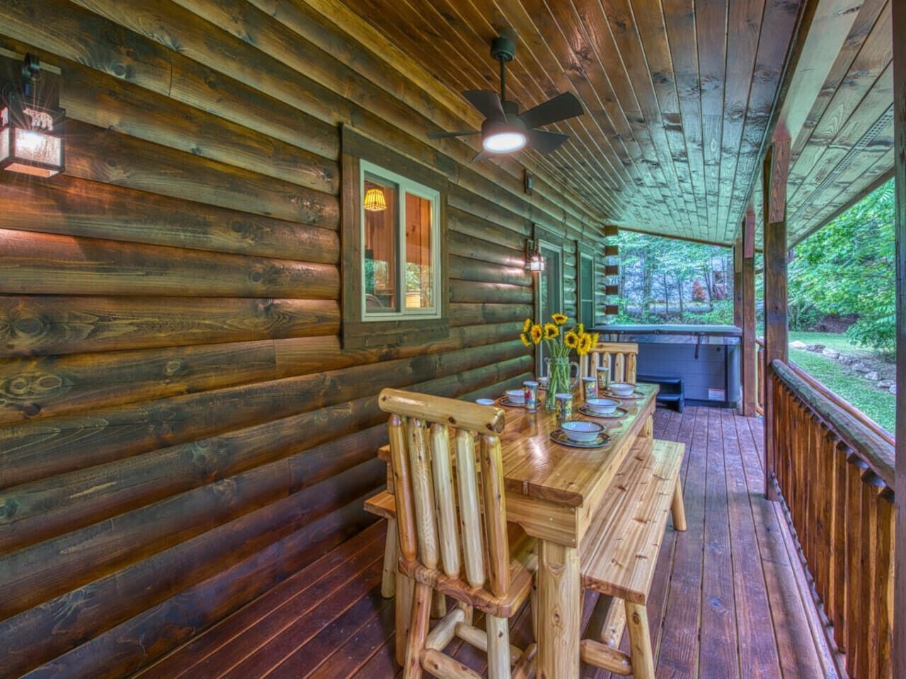 A wooden cabin with a covered porch, a dining table with chairs, and a view of the surrounding forest.