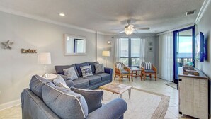 A living room with a sofa, chairs, a coffee table, a ceiling fan, and a view through a glass door. - 308 Summerhouse by Avantstay Oceanview Condo w/ Community Pool Access (Isle of Palms)
