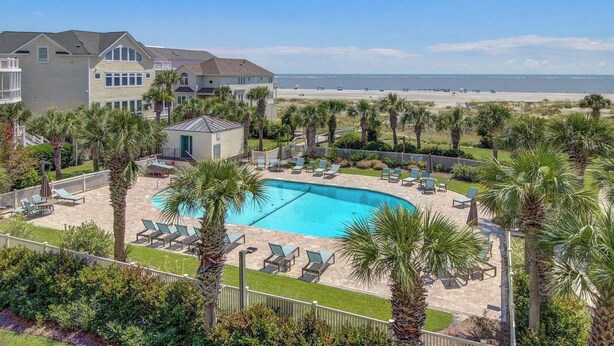 A pool with lounge chairs, a small building, and a beach in the background. - 308 Summerhouse by Avantstay Oceanview Condo w/ Community Pool Access (Isle of Palms)