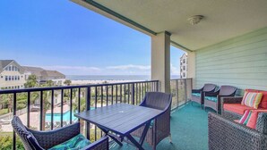 A balcony with a table and chairs, a view of a swimming pool, and a building in the background. - 308 Summerhouse by Avantstay Oceanview Condo w/ Community Pool Access (Isle of Palms)