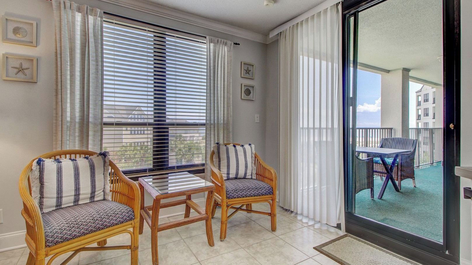 A balcony with wicker furniture, a glass table, and a view of buildings.
