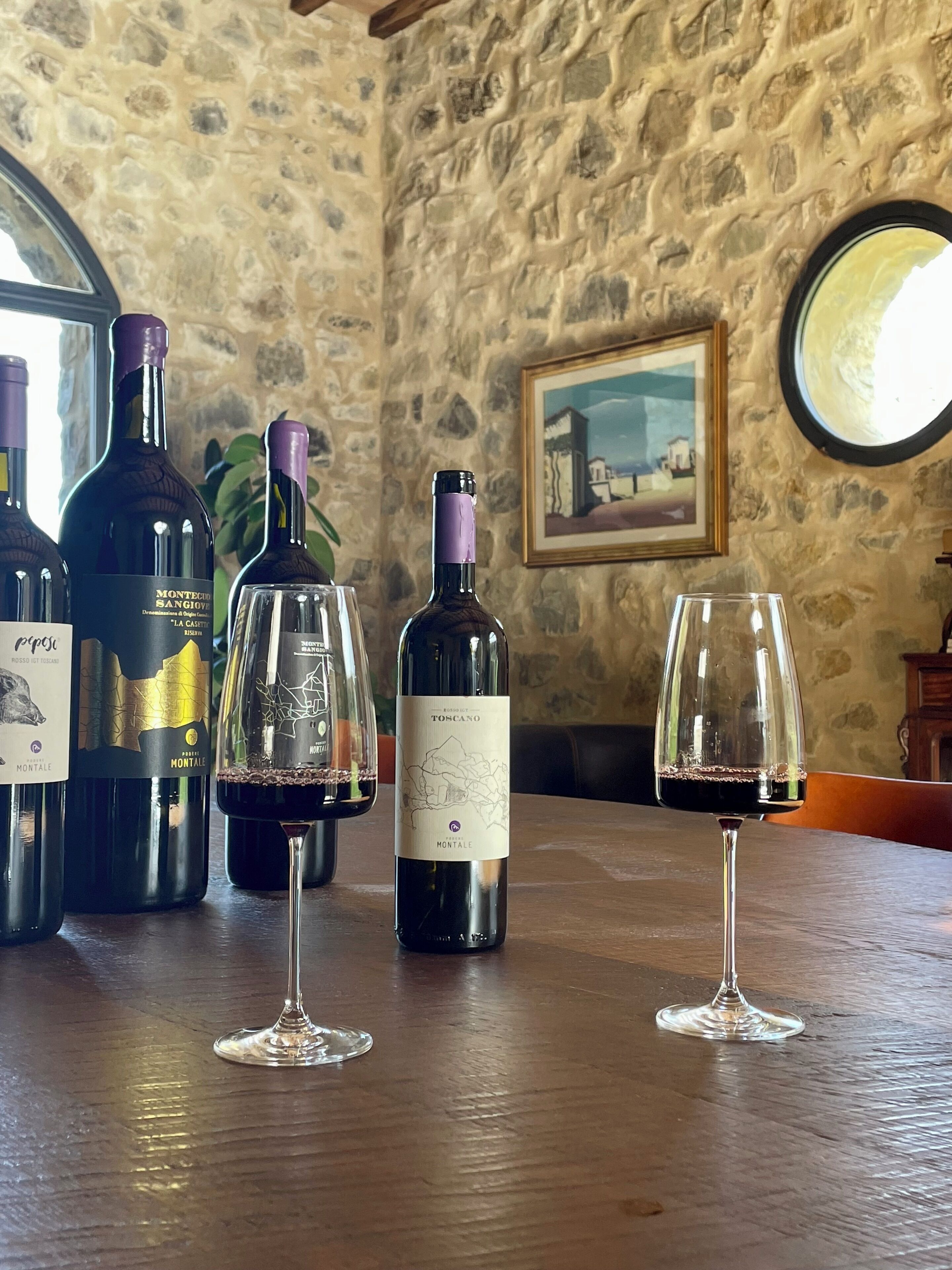 Un intérieur avec un mur en pierre, des bouteilles de vin et des verres disposés sur une table en bois.