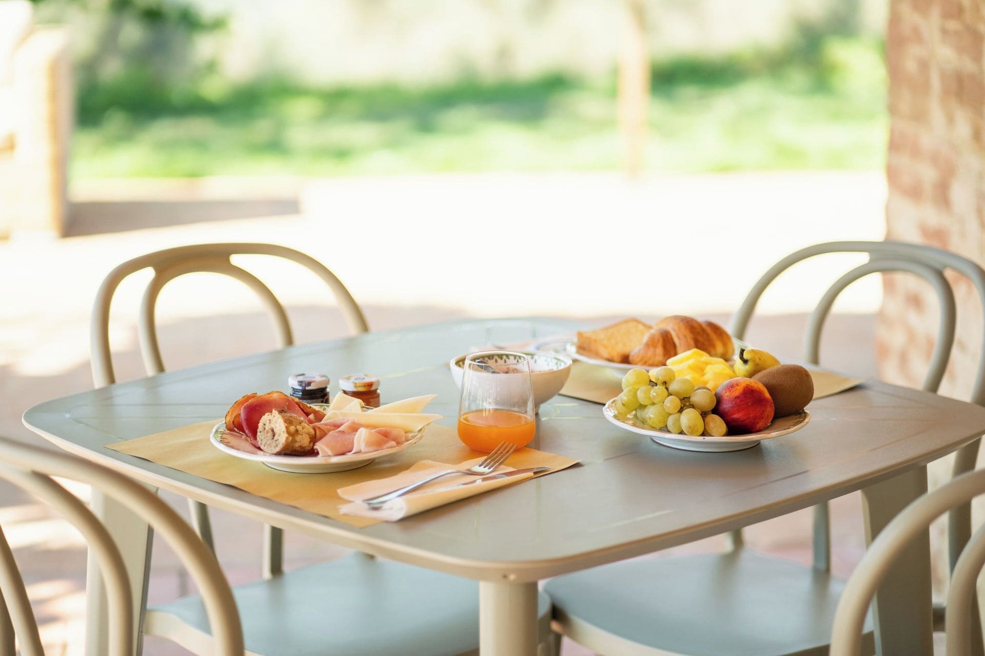 A breakfast table with croissants, fruit, cheese, and a glass of orange juice.