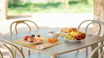 A breakfast table with croissants, fruit, cheese, and a glass of orange juice.