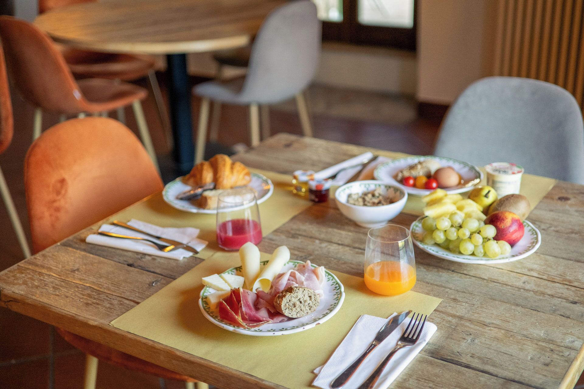 A breakfast table with plates of food, including croissants, cheese, ham, grapes, and a glass of orange juice.