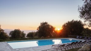 Une piscine rectangulaire, bordée d’une terrasse carrelée, entourée de chaises longues et d’une rambarde en métal.