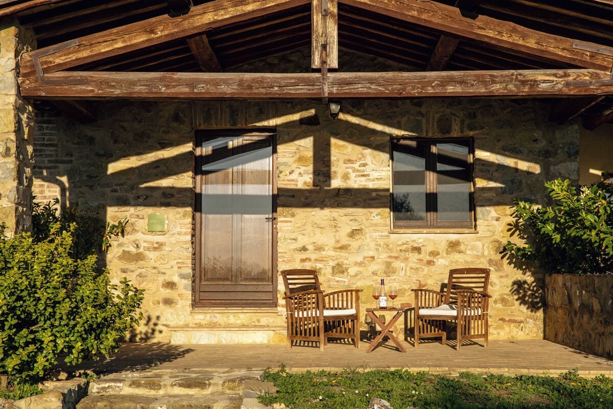 A rustic stone building with wooden beams, two wooden chairs, a small table, and a bottle of wine.