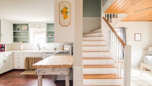 A kitchen with wooden flooring, a dining table, and a staircase with white railings. - Walk to Main! Hot Tub, Fire Pit, Texas Charm (Fredericksburg)