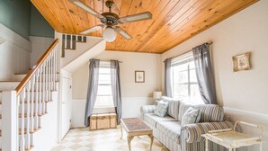 A room with a checkered floor, a striped sofa, a wooden ceiling fan, and a staircase with white railings. - Walk to Main! Hot Tub, Fire Pit, Texas Charm (Fredericksburg)
