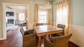 A dining area with a wooden table and wicker chairs, a fireplace, and a television in the background. - Walk to Main! Hot Tub, Fire Pit, Texas Charm (Fredericksburg)