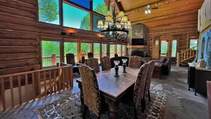 A log cabin interior with a dining area, large windows, a fireplace, and a staircase. - Beautiful Log Cabin 3 Miles to Purgatory Ski Resort with Private Hot Tub (Durango)
