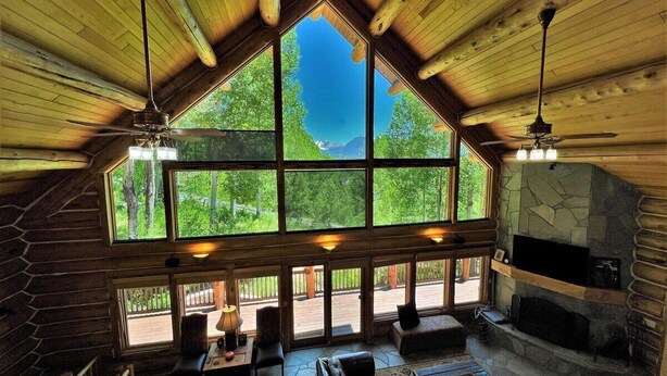 A log cabin interior with a large skylight, stone fireplace, and outdoor deck. - Beautiful Log Cabin 3 Miles to Purgatory Ski Resort with Private Hot Tub (Durango)