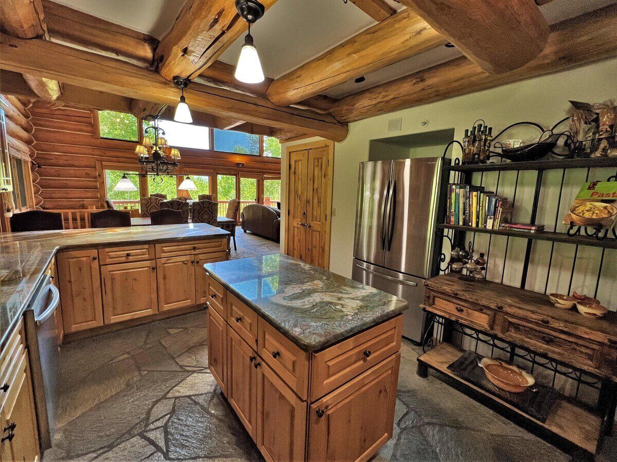 A rustic kitchen with wooden cabinets, a granite countertop, and a stainless steel refrigerator.