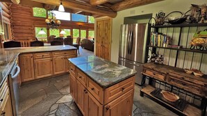 A rustic kitchen with wooden cabinets, a granite countertop, and a stainless steel refrigerator. - Beautiful Log Cabin 3 Miles to Purgatory Ski Resort with Private Hot Tub (Durango)
