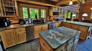 A spacious kitchen with wooden cabinets, a marble countertop, and a large island. - Beautiful Log Cabin 3 Miles to Purgatory Ski Resort with Private Hot Tub (Durango)