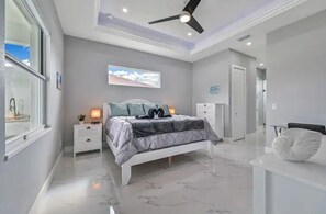 Une chambre moderne avec un lit, des tables de chevet, un ventilateur de plafond et une grande fenêtre.