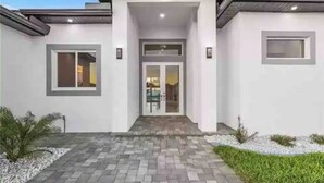 A modern house with a central entrance, a paved driveway, and a well-maintained lawn.