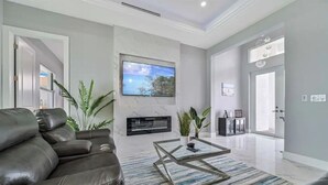 A modern living room with a leather sofa, a flat-screen TV mounted on a marble wall, a fireplace, and a large window.
