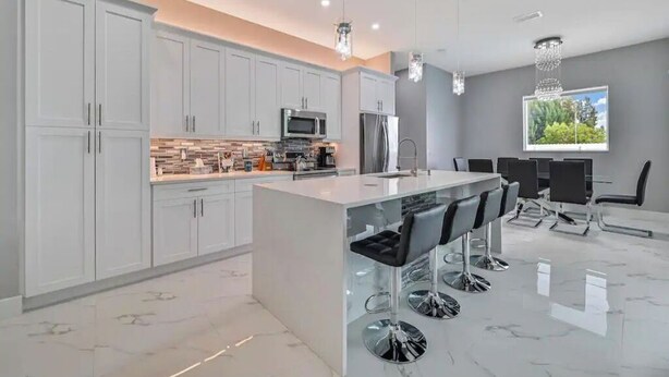 A modern kitchen with white cabinets, a central island with bar stools, stainless steel appliances, and pendant lighting.