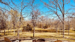 A campsite with two Adirondack chairs facing a fire pit, surrounded by trees and a clear sky. - Cozy tiny cabin, kitchenette, private pond for fishing, near lake (Ringold)