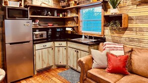 A compact kitchen with a refrigerator, microwave, and built-in oven. There is a sink, a window with blinds, and a wooden ceiling. - Cozy tiny cabin, kitchenette, private pond for fishing, near lake (Ringold)