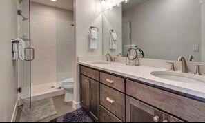 A modern bathroom with a glass shower enclosure, two sinks, a large mirror, and dark wooden cabinetry.